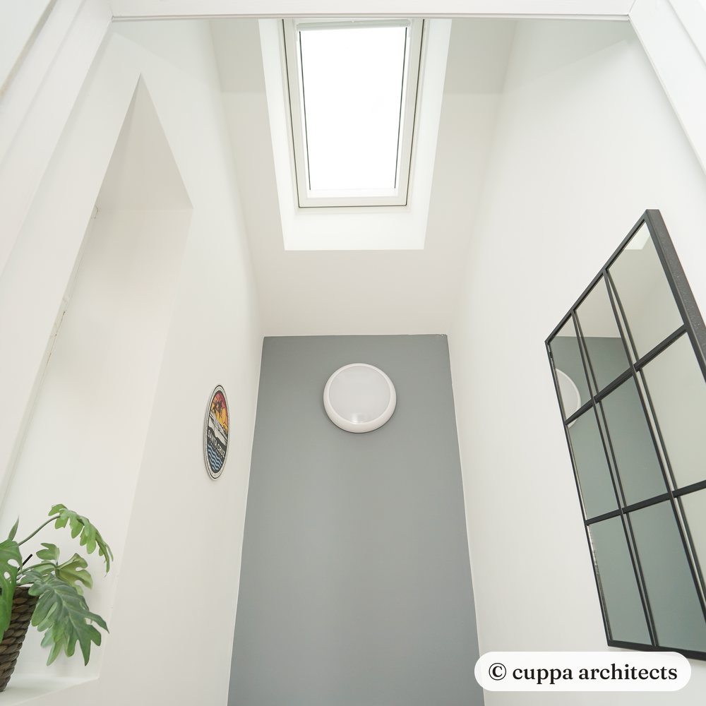 A rooflight pouring daylight down white walls beside a window-style mirror