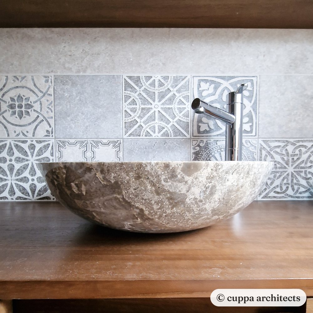 A stone vessel basin on a timber vanity against patterned tiles