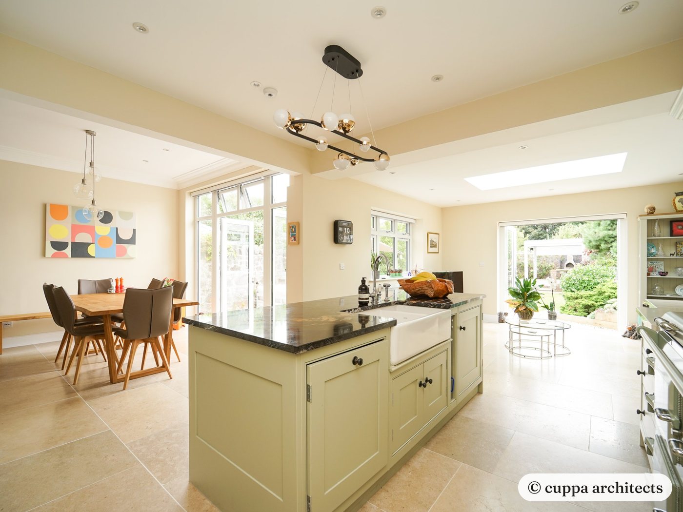 An open-plan kitchen and dining room with a painted island, stone floor and doors to the garden