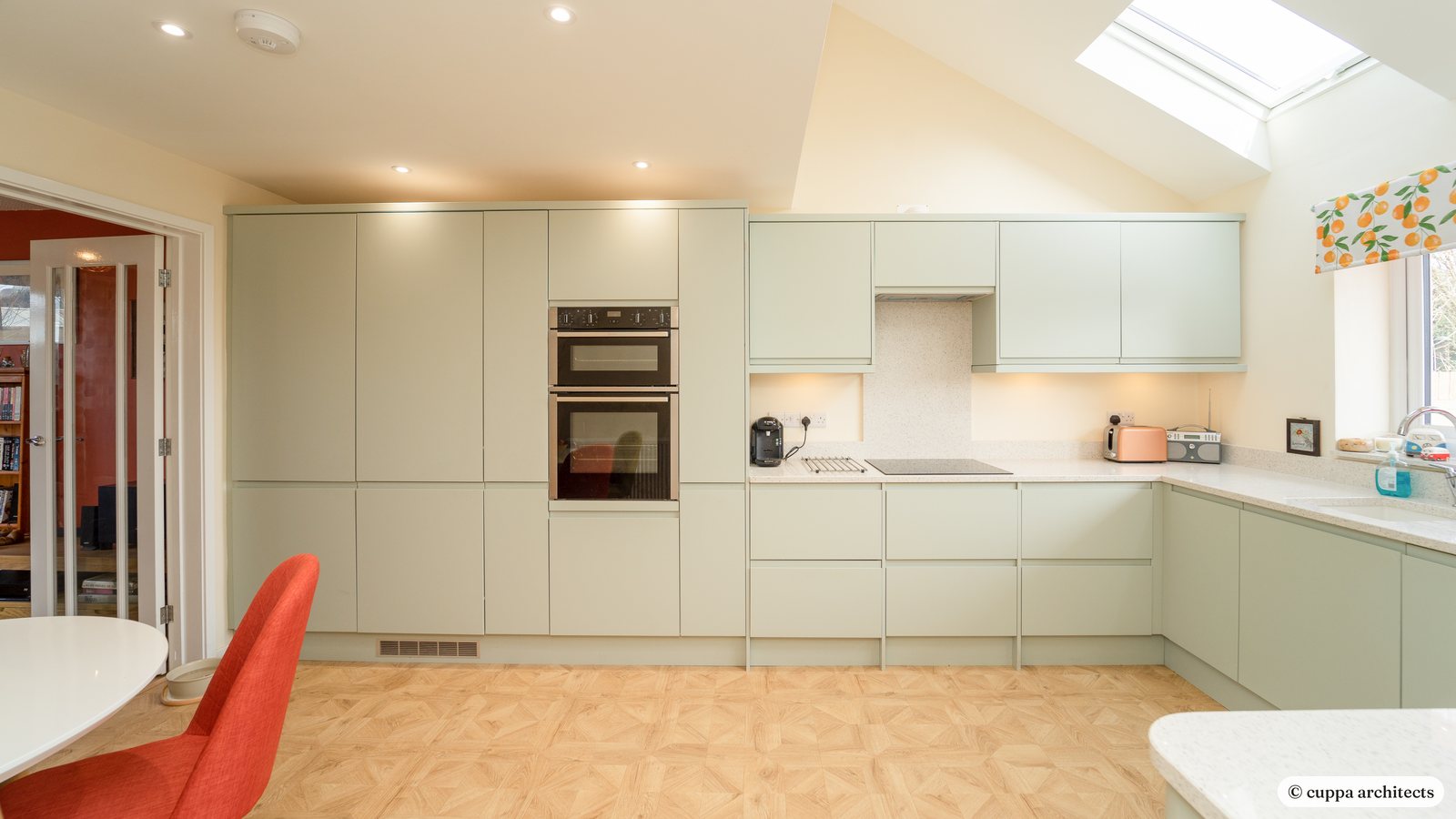 A bright kitchen in a converted garage with sage green units, a vaulted ceiling and roof windows
