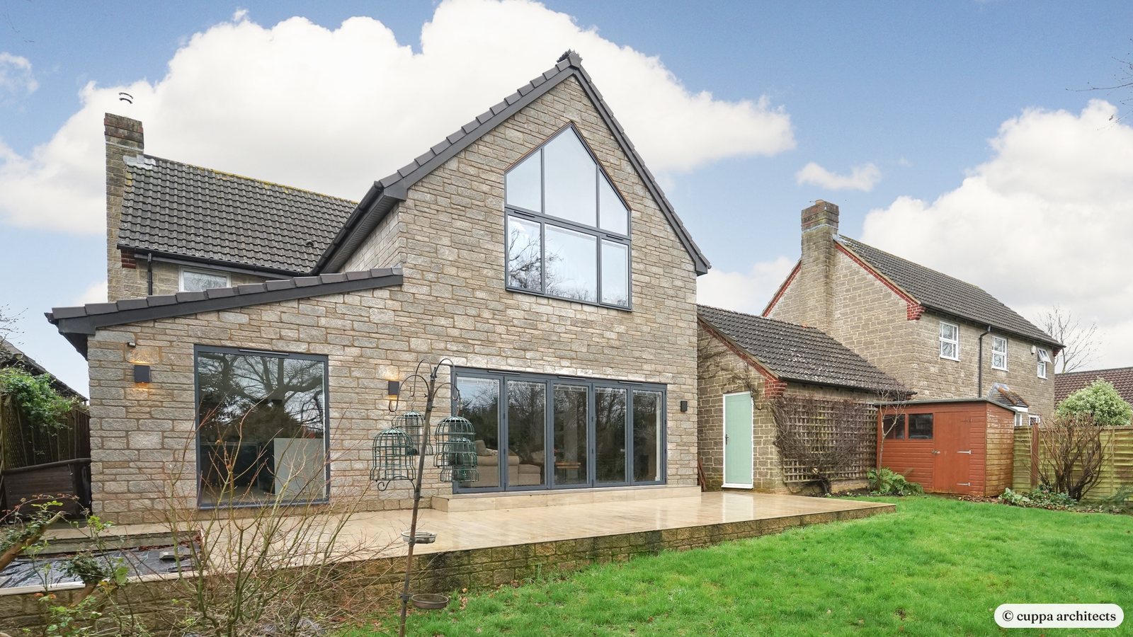 The rear of a stone house with a new extension and a fully glazed gable