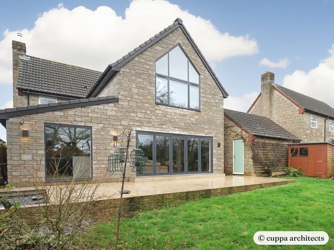 The rear of a stone house with a new extension and a fully glazed gable